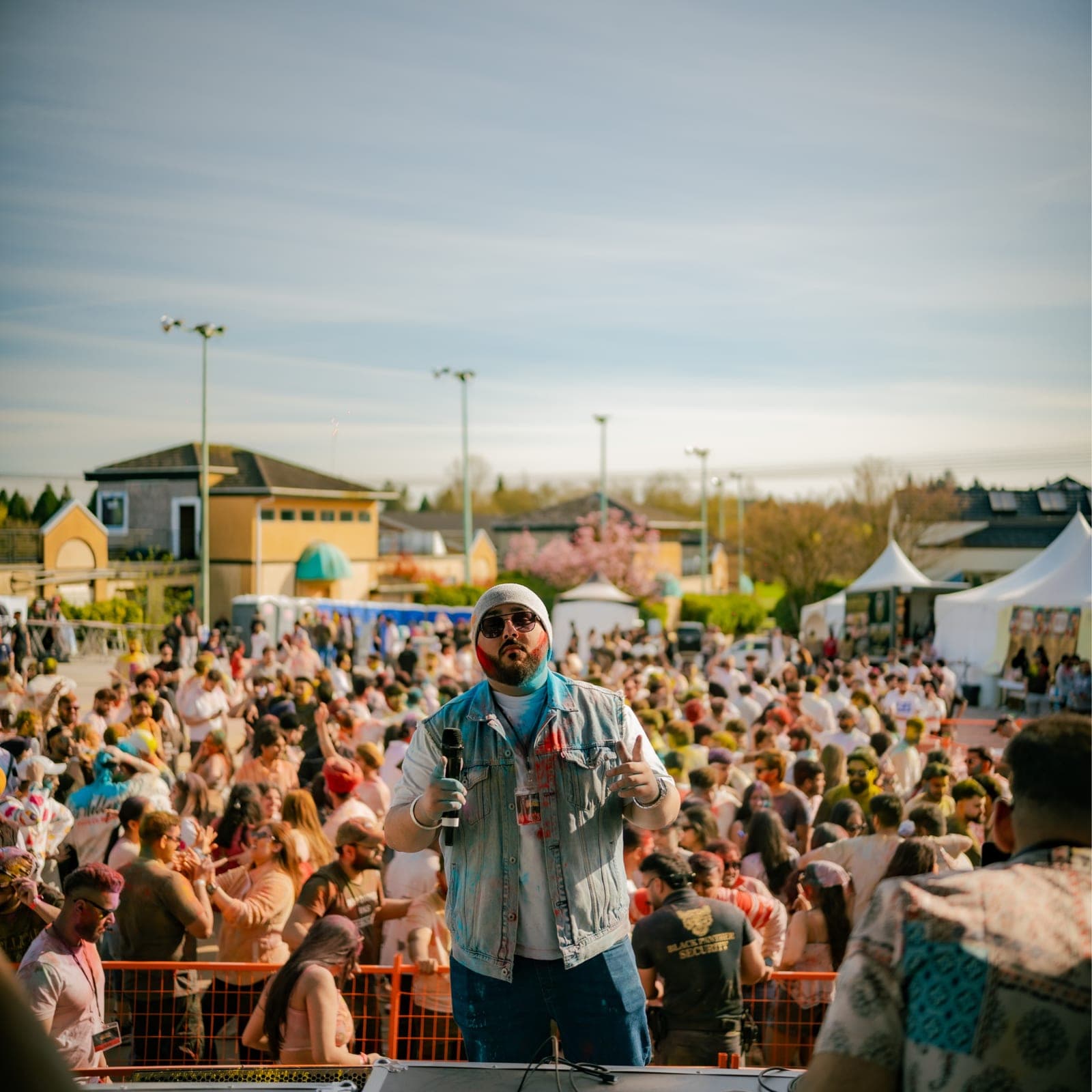 MC on stage in front of a colour-dusted crowd at Chaska's outdoor Holi festival